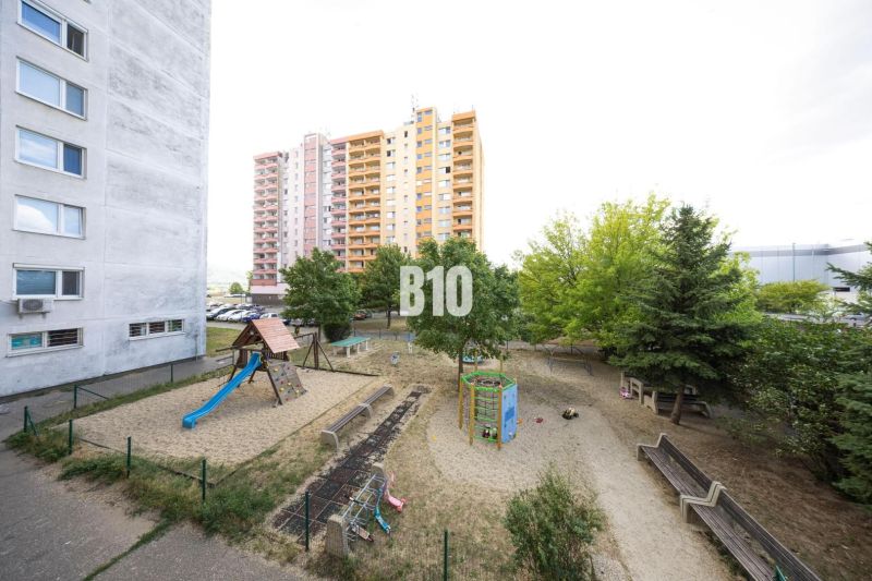 A children's playground in Bratislava IV near a panel building, a 3-room apartment in the background.