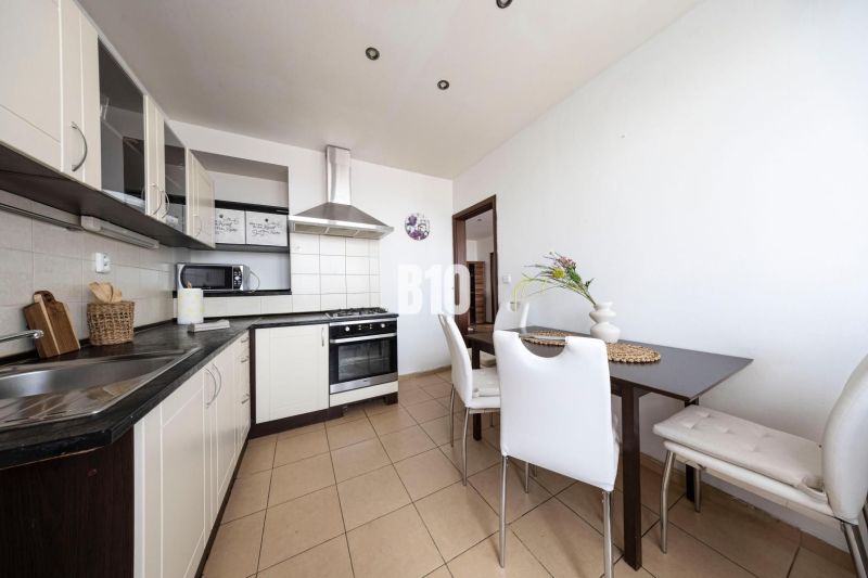 A kitchen in a 3-room apartment with white cabinets, a dining table, and appliances.