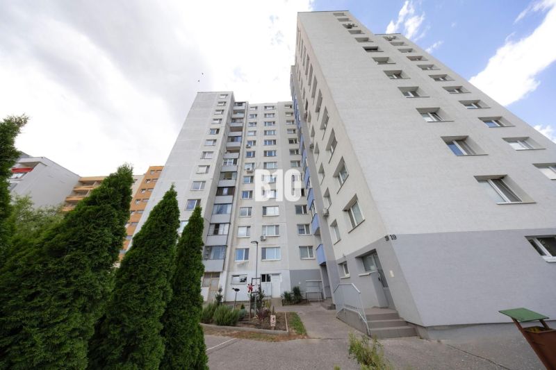 A large apartment building in Bratislava IV surrounded by greenery and sky.