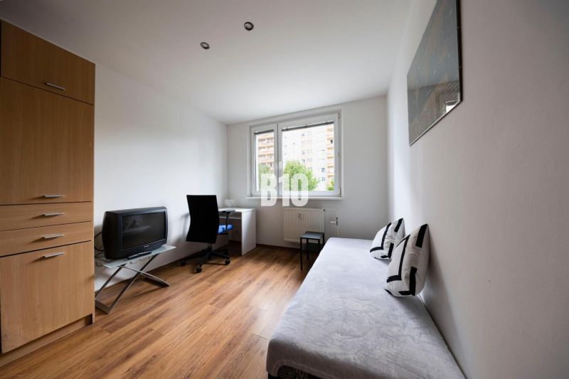 A room in a 3-room apartment with a wooden decor floor, a sofa, and a desk.