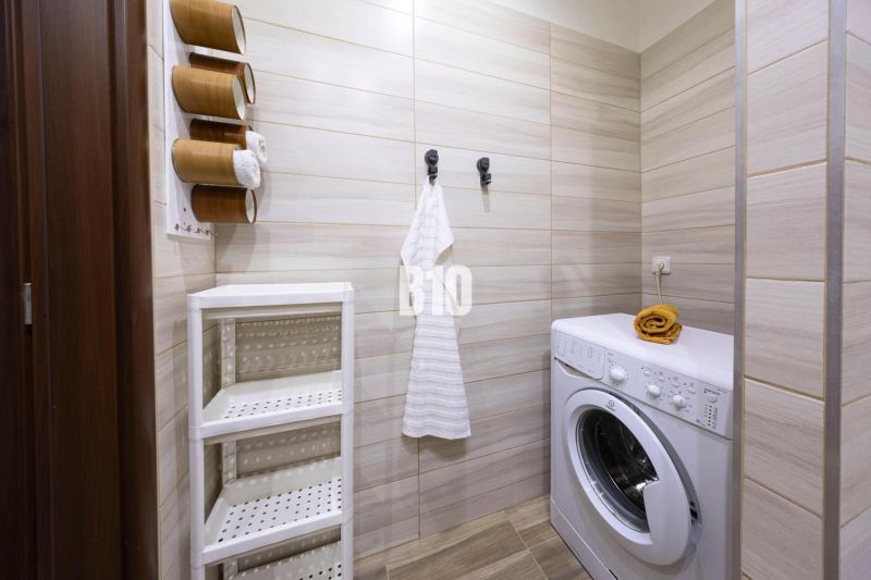 A bathroom with a washing machine and a shelving storage system in a three-room apartment.