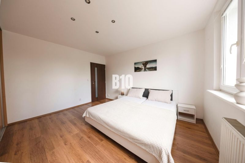 Bedroom with a double bed, wood-patterned flooring, and white walls in a three-room apartment.