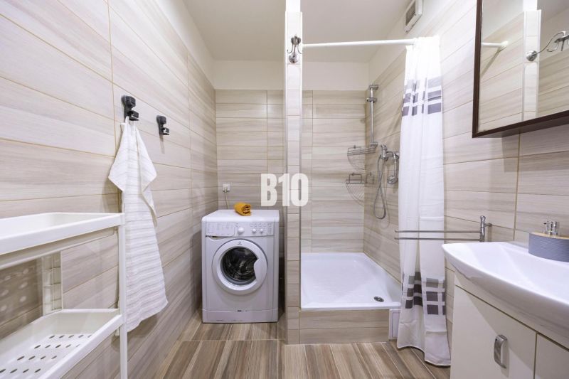 Bathroom with a washing machine, shower cabin, and white sink in a 3-room apartment.