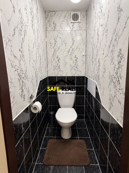 A toilet in a 3-room apartment with patterned walls and dark tiles.