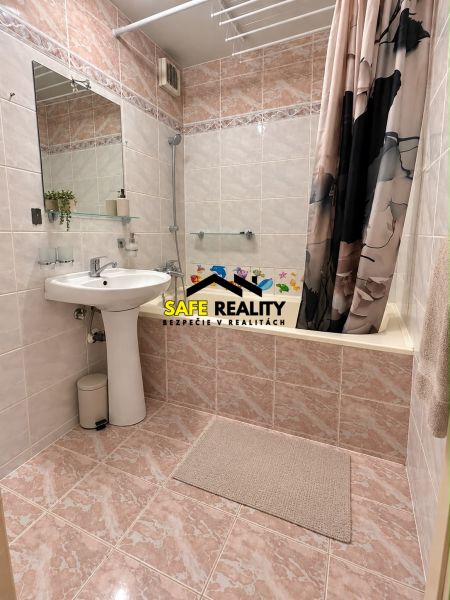 Bathroom in a three-room apartment with a bathtub, sink, large mirror, and tiles.