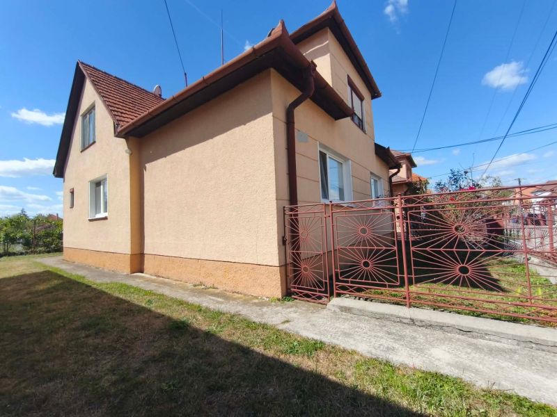 A family house in Oslany with a red roof and a wrought iron gate on the property.
