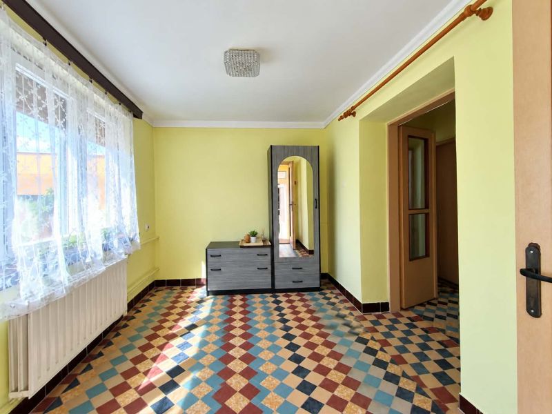 A room with a patterned floor, light yellow walls, and a window with curtains in a family house.