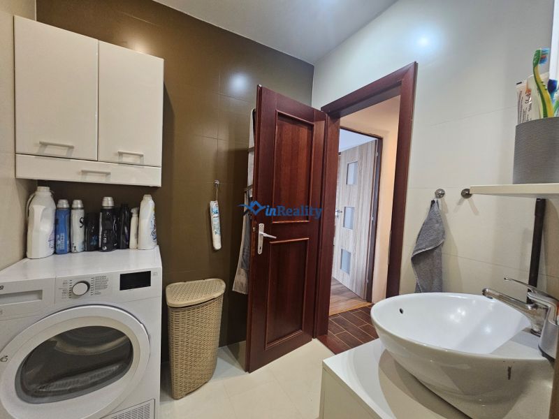 Bathroom in a 4-room apartment with a washing machine, sink, and dark brown doors.
