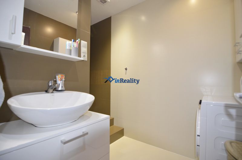 A bathroom with a sink, cabinet, shelf, and washing machine in a 4-room apartment.