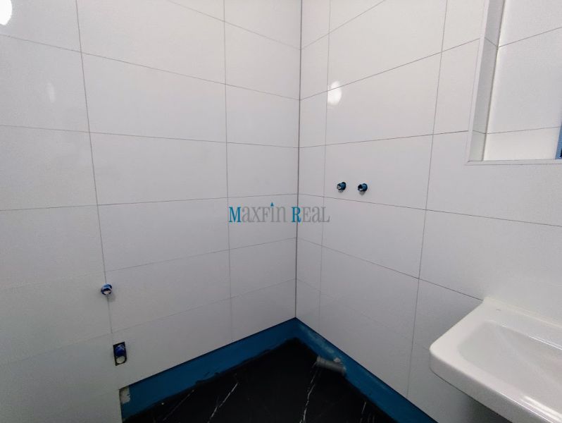 White tiles on the walls and a dark floor in the office bathrooms.