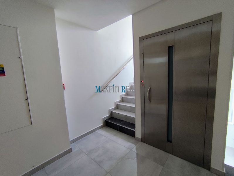 Elevator and stairs in offices with white walls and tiles.