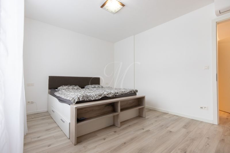A bedroom with a bed, white walls, and a floor with a wooden decor in a 2-room apartment.