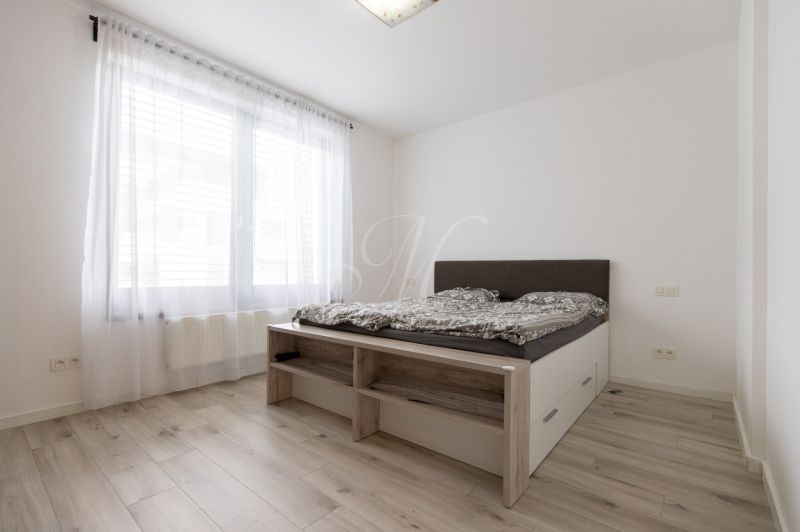 A bright bedroom with retractable curtains, a bed, and a wooden decor floor in a 2-room apartment.