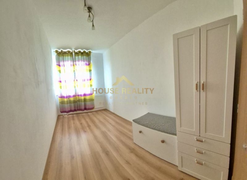 A bright room with a wood-patterned floor in a three-room apartment, a white wardrobe, colorful curtains.