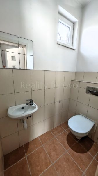 A bathroom in a family house with a toilet, a sink, and a window, simple tiles.