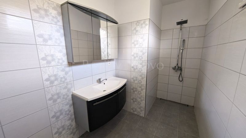 A bathroom with white tiles and a shower enclosure, without a shower tray, in a family house.