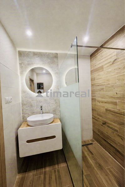 Bathroom with a sink, mirror, and shower, floor with wooden decor, 3-room apartment.