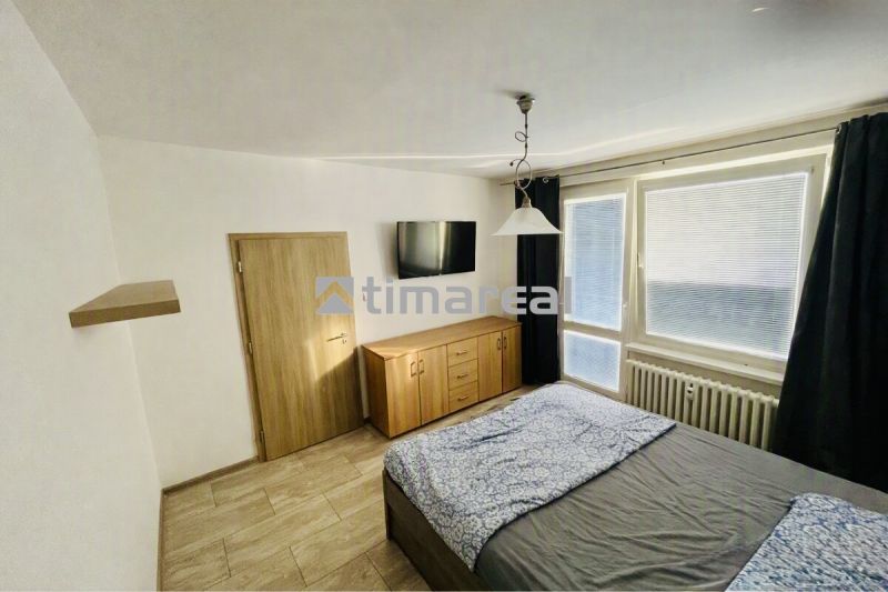A bedroom with a wood-patterned floor, a bed, a dresser, and a television in a 3-room apartment.