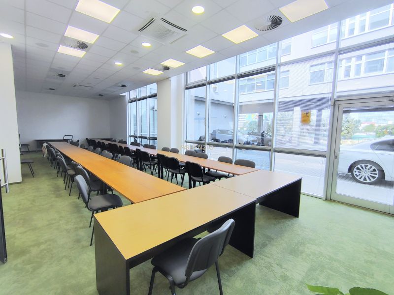 Commercial spaces with large windows, long tables and chairs, green carpet.