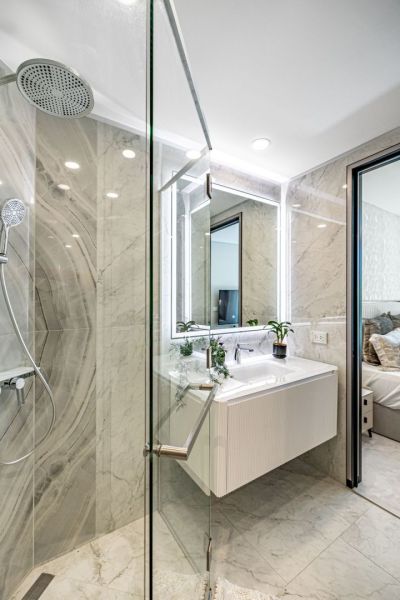 A bathroom with a glass shower enclosure, marble walls, and a white sink in a vacation apartment.