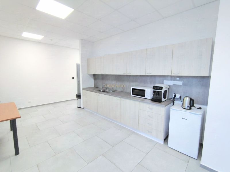 Offices with a bright kitchenette, cabinets, microwave oven, and refrigerator, with tiles on the floor.