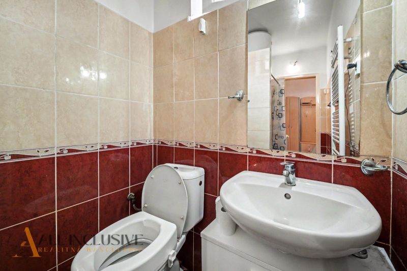A bathroom in a family house with a toilet and a sink, tiled with red and beige tiles.