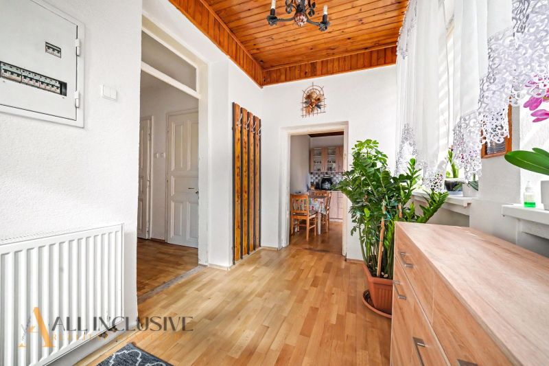 A hallway in a family house with a wooden decor floor, plants, and a view into the kitchen.