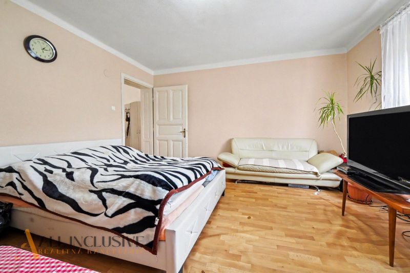 Bedroom with a bed, couch, television, and wooden decor flooring in a family house.