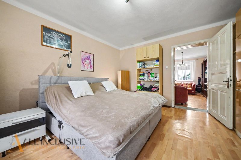A bedroom in a family house with a wooden decor floor, equipped with a bed and shelves.