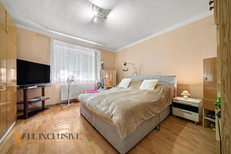 Bedroom in a family house with wood-patterned flooring, a television, and a bed.
