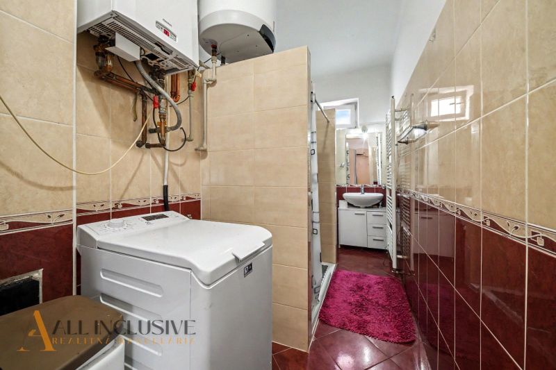 Bathroom in a family house with a washing machine and a shower, surrounded by tiles.