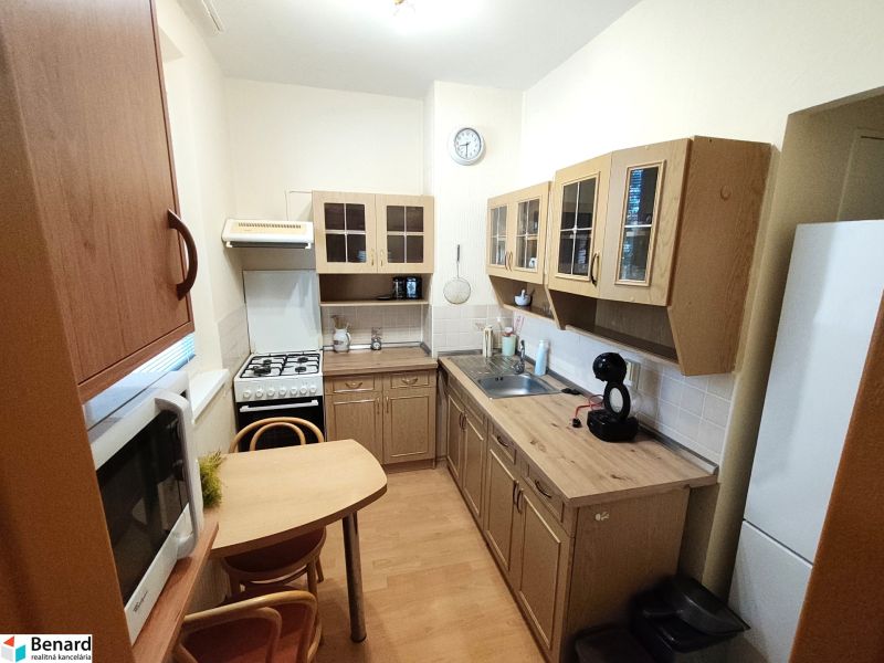 A kitchen in a studio apartment with a wooden decor floor, table, chairs, appliances.
