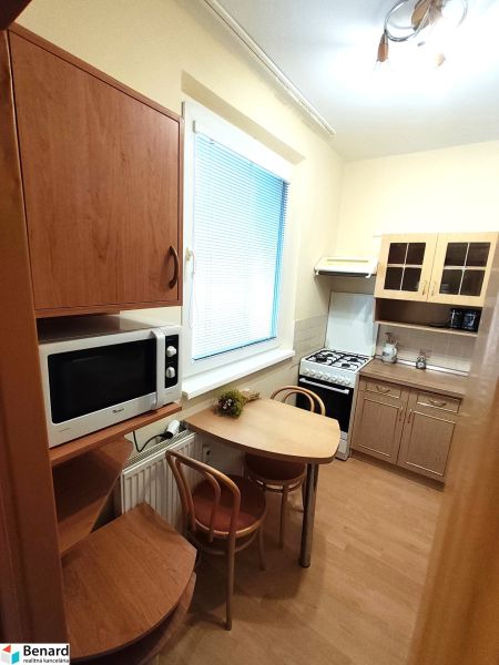 A kitchen in a studio apartment with a wooden decor floor, includes a table, microwave, and stove.