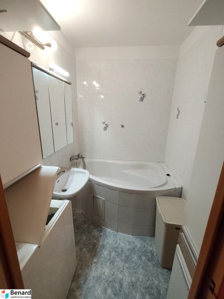 Bathroom in a one-room apartment with a bathtub, mirror, and storage cabinets.