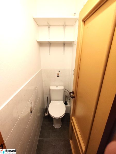 A compact toilet with hanging shelves and light tiles in a studio apartment.