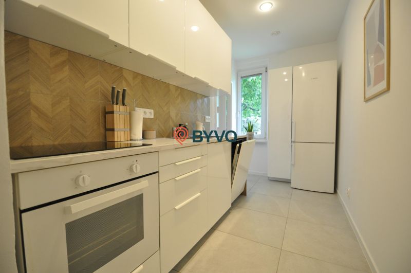 A kitchen in a 2-room apartment with white cabinets and a backsplash with a wooden decor.
