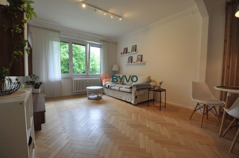 Living room in a two-room apartment with a sofa, large windows, and a wooden decor floor.