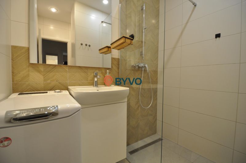A bathroom with a shower, sink, and washing machine in a 2-room apartment.