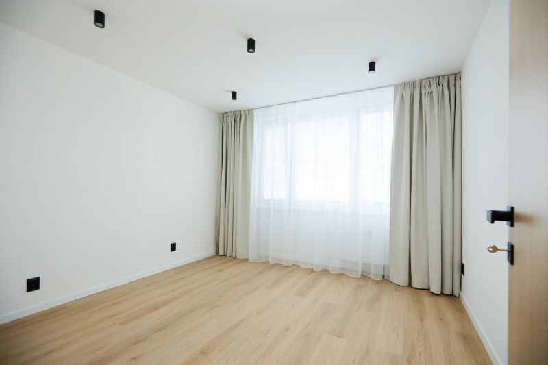 A room in a 2-room apartment with a wood-decor floor and white curtains.