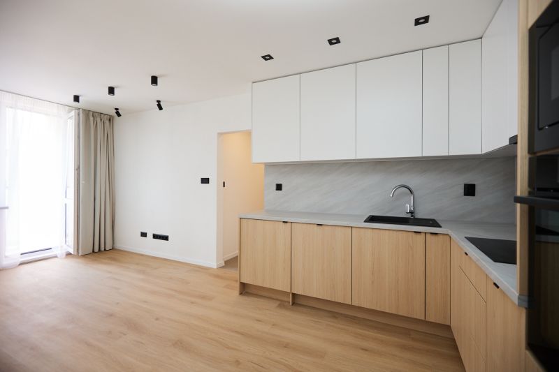 A kitchen space in a 2-room apartment with a wooden decor floor and white cabinets.