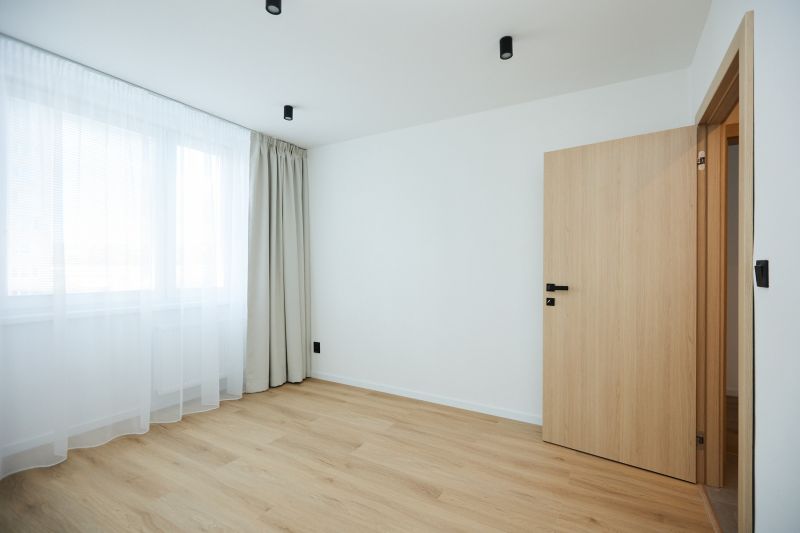 An empty room with a wood-patterned floor and a window with curtains in a two-room apartment.