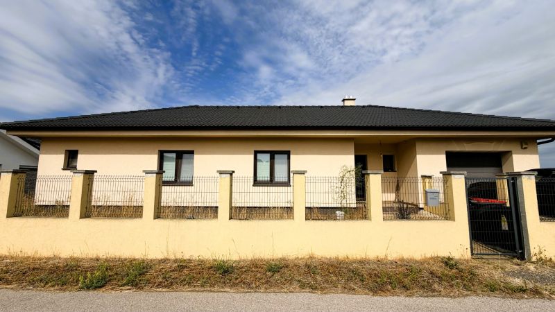 A family house in Nickelsdorf with a white facade and a black roof behind a fence.