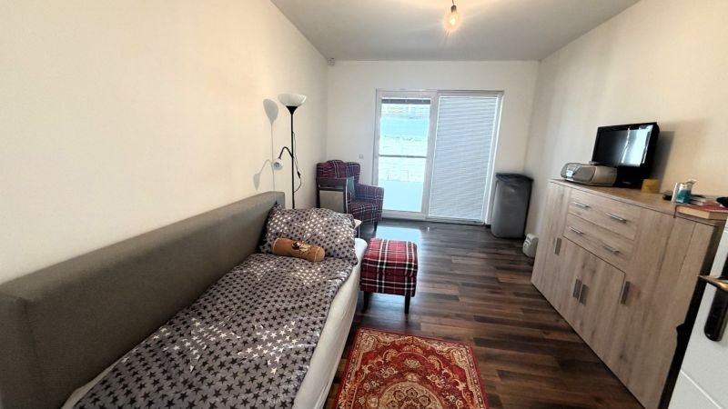 A room in a family house with a bed, an armchair, and a floor with a wood decor.
