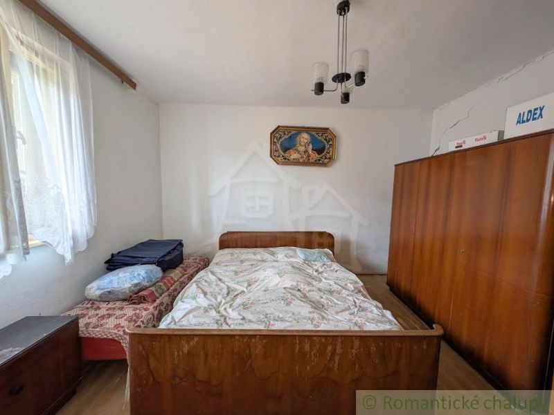 A bedroom in a family house with wooden wardrobes and a bed, delicate curtains on the window.
