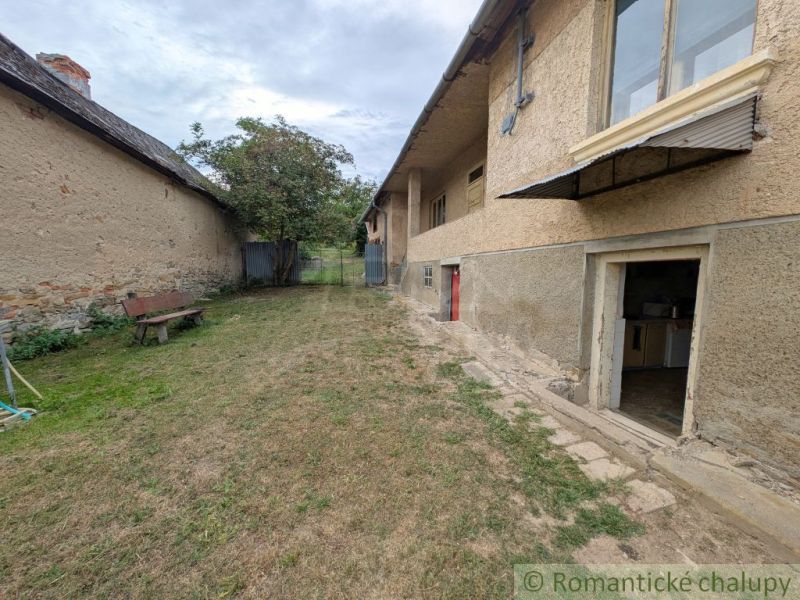 The courtyard of a family house in Nižné Ladičkovce with a bench and lawn, next to a stone wall.