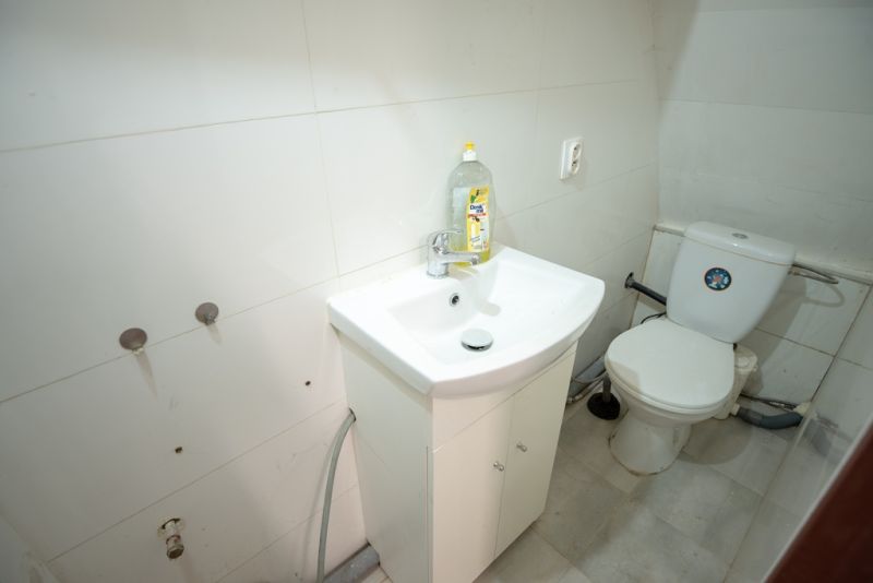 A bathroom in a family house with a sink and a toilet, simple white tiles.
