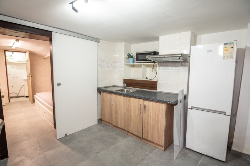 A kitchen in a family house with a refrigerator, sink, and light ceramic tiles.