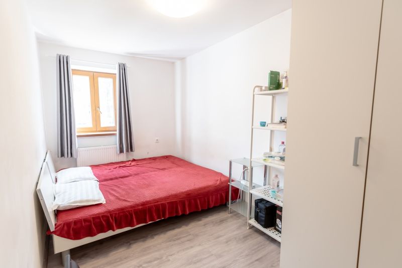 A bedroom in a family house with a red bed and a shelf. Floor with wooden decor.