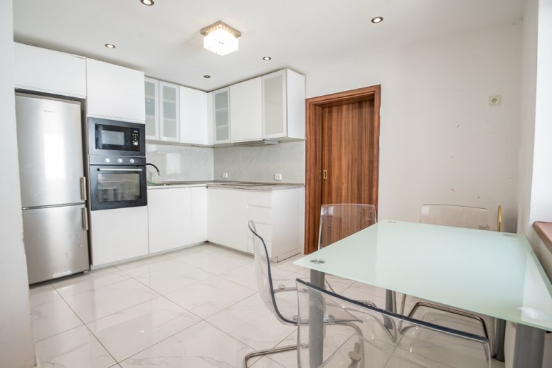 A kitchen in a family house with a glass table, cabinets, and appliances, flooring with a white decor.
