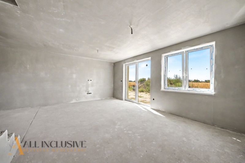 A spacious room in a family house with large windows and an unfinished floor.